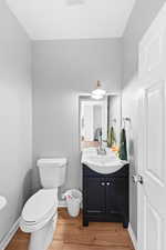 Half bathroom with baseboards, wood finished floors, toilet, and vanity