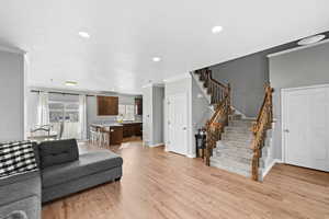 Living room with crown molding, light wood finished floors, baseboards, recessed lighting, and stairway
