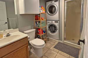 Main level bathroom with stacked washer / dryer, a shower stall, toilet, tile patterned floors, and vanity
