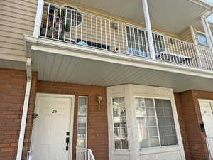Front doorway to property with a balcony, brick siding, and a porch