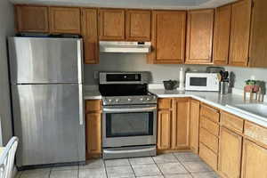 Kitchen featuring under cabinet range hood, light countertops, brown cabinets, and stainless steel appliances