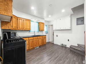 Kitchen featuring dark wood-style flooring, stainless steel microwave, dark countertops, a sink, and black range with gas cooktop