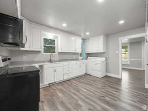 Kitchen with a sink, black microwave, electric range oven, light wood-type flooring, and washer and dryer