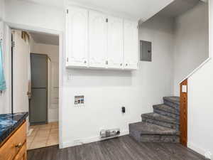 Washroom with electric panel, hookup for a washing machine, baseboards, and wood finished floors