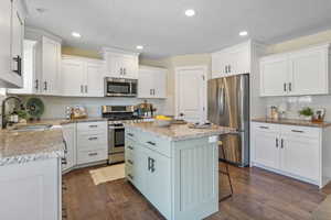 Kitchen with dark wood-style flooring, white cabinets, appliances with stainless steel finishes, a sink, and a center island