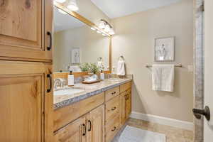 Primary Suite bathroom featuring tile patterned floors, a sink, double vanity, and baseboards