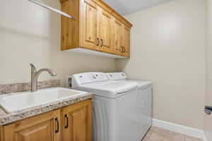 Washroom featuring baseboards, washing machine and dryer, cabinet space, and a sink
