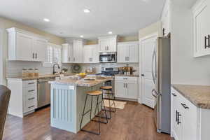 Kitchen featuring a sink, a breakfast bar area, appliances with stainless steel finishes, dark wood finished floors, and white cabinets