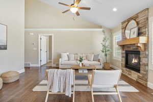 Living area featuring baseboards, wood finished floors, a ceiling fan, and a stone fireplace