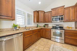 Kitchen with brown cabinets, stainless steel appliances, lofted ceiling, a sink, and light tile patterned floors