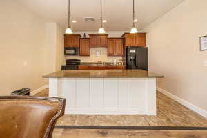 Kitchen with visible vents, brown cabinets, a kitchen island, a sink, and black appliances