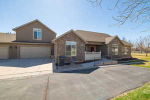 View of front of home with stone siding, central AC unit, a garage, concrete driveway, and stucco siding
