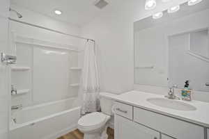 Bathroom with toilet, vanity, wood finished floors, shower / bath combo with shower curtain, and visible vents