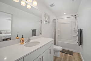 Ensuite bathroom featuring toilet, vanity, wood finished floors, visible vents, and shower / bath combination with curtain