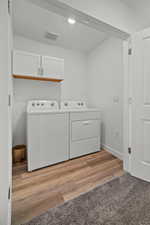 Laundry area with baseboards, light wood-type flooring, washing machine and clothes dryer, and cabinet space