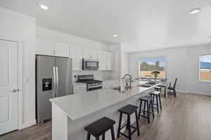 Kitchen with a breakfast bar, white cabinetry, a sink, and stainless steel appliances