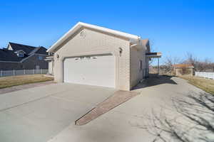 View of property exterior featuring brick siding, driveway, a garage, and fence