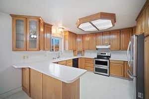 Kitchen featuring light countertops, a sink, a peninsula, under cabinet range hood, and stainless steel appliances