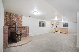 Unfurnished living room featuring light carpet, baseboards, and a wood stove