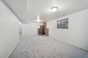 Finished basement with a textured ceiling, visible vents, baseboards, carpet floors, and a wood stove