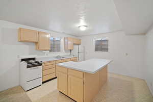 Kitchen with light countertops, a sink, light brown cabinetry, and white appliances