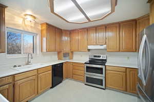 Kitchen featuring light countertops, light floors, appliances with stainless steel finishes, under cabinet range hood, and a sink