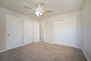 Unfurnished bedroom featuring baseboards, carpet flooring, a ceiling fan, and two closets