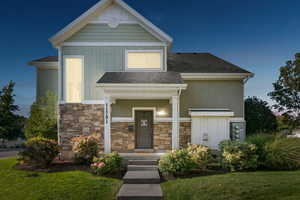 View of front of house featuring a front lawn, stone siding, board and batten siding, and roof with shingles