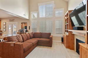 Living area with light wood-type flooring, baseboards, a high ceiling, visible vents, and a tiled fireplace
