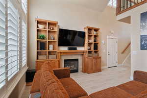 Living room featuring stairway, light wood-type flooring, baseboards, a towering ceiling, and a tile fireplace