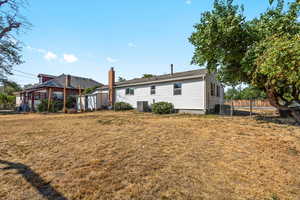 Rear view of house with central air condition unit, a chimney, fence, and a yard