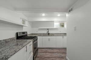 Kitchen with white cabinetry, open shelves, stainless steel range with gas cooktop, a sink, and visible vents