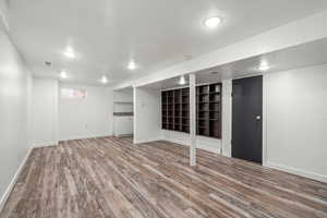 Basement with visible vents, a textured ceiling, baseboards, and wood finished floors