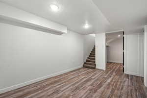 Finished below grade area featuring baseboards, wood finished floors, stairway, and a textured ceiling