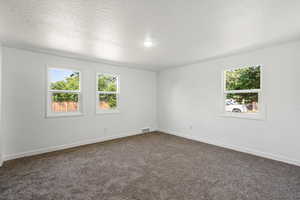 Spare room featuring baseboards, visible vents, dark carpet, and a healthy amount of sunlight