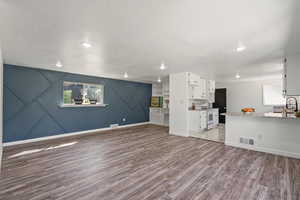 Unfurnished living room featuring baseboards, a textured ceiling, a sink, light wood-style floors, and visible vents