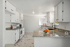 Kitchen featuring light stone countertops, electric range, marble finish floor, a sink, and a peninsula