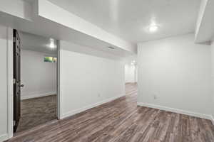 Finished below grade area with baseboards, visible vents, a textured ceiling, and wood finished floors