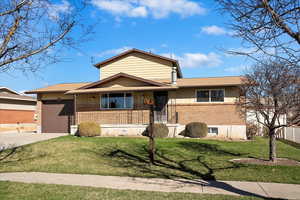 View of front of property with fence, a garage, concrete driveway, brick siding, and a front lawn