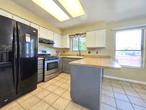 Kitchen featuring black fridge, gas range, under cabinet range hood, a peninsula, and a sink