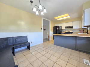 Kitchen featuring a sink, stainless steel gas range, light countertops, under cabinet range hood, and white cabinetry