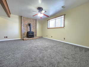 Unfurnished living room with a wood stove, a ceiling fan, carpet floors, baseboards, and a textured ceiling