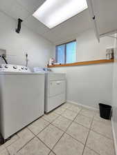 Washroom with independent washer and dryer, light tile patterned floors, and baseboards
