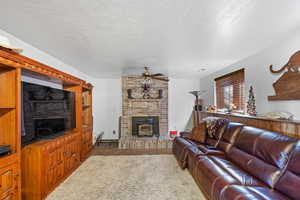 Living room with a wood stove, ceiling fan, carpet flooring, and a textured ceiling