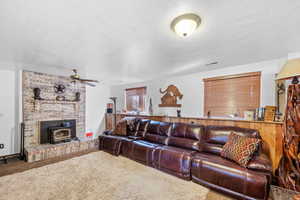 Living room with carpet floors, a wood stove, a textured ceiling, visible vents, and ceiling fan