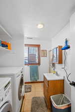 Washroom with a textured ceiling, a sink, washer and clothes dryer, cabinet space, and light tile patterned floors