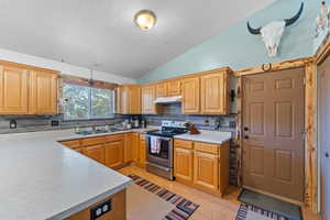 Kitchen featuring vaulted ceiling, light countertops, a sink, under cabinet range hood, and stainless steel electric range oven