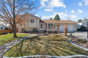 Tri-level home featuring driveway, a front yard, an attached garage, fence, and brick siding