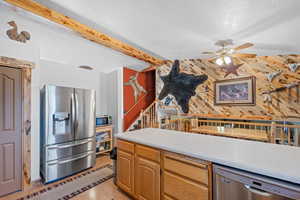 Kitchen with light countertops, appliances with stainless steel finishes, beamed ceiling, light wood-style floors, and ceiling fan