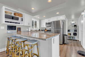 Kitchen with white cabinets, a peninsula, stainless steel appliances, and light stone countertops